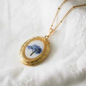 Detailansicht der goldenen ovalen Medaillon-Kette mit blauen Trockenblumen im Retro-Stil
