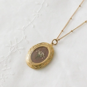 Detail eines 14k Gold-Medaillons mit echten weißen Trockenblumen und vintage Satellitenkette