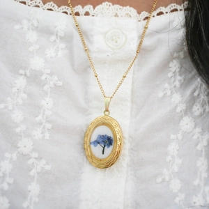 Detailansicht eines 14k Gold Medaillons mit blauen Blumenakzenten und einer feinen Perlenkette