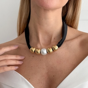 Detail van de stoffen knoopketting met parel en gouden kralen op zwart textiel koord