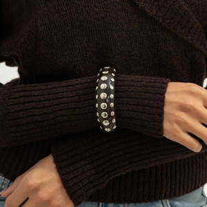 Detailed view of punk resin bangle with silver rivets on amber brown textured surface