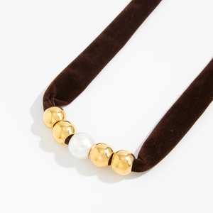 Detailopname van de fluwelen halsketting met gouden metalen kralen en een witte parel accent