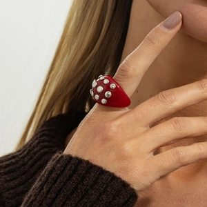 Detailed view of bulky red resin ring with silver spherical rivets worn on the finger