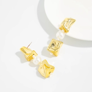Gros plan de boucles d'oreilles dorées irrégulières avec glands de perles blanches