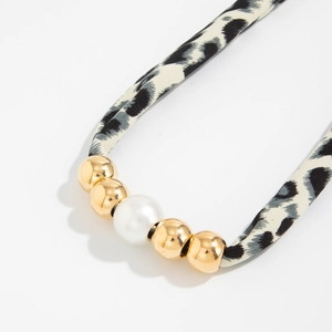 Detail van luipaardprint stoffen knoopketting met gouden metalen kralen en witte imitatieparel