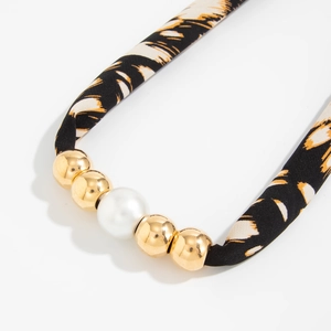 Macro-detail van luipaardprint stoffen band met gouden kralen en witte parelketting