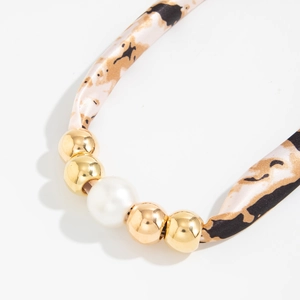Detail van geknoopte luipaardprint ketting met gouden kralen en een witte parel