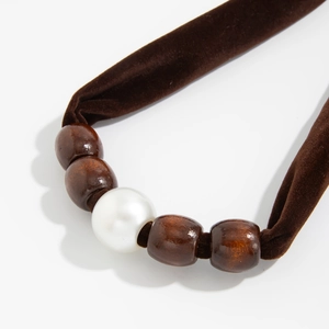 Detail van donkerbruine fluwelen ketting met houten kralen en een witte imitatieparel