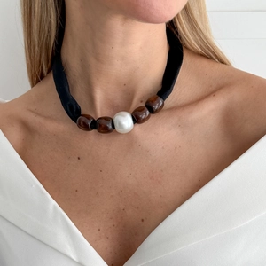 Detailopname van de zwarte stoffen choker met bruine kralen en grote parel op nek