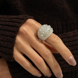 Detail of cream resin ring with inlaid crystals worn over a brown knit sweater