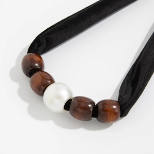 Macro-detail van zwarte fluwelen choker met vintage houten kralen en centrale parel