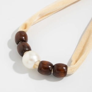 Detail van beige fluwelen ketting met bruine houten kralen en een grote imitatieparel