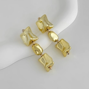 Détail de boucles d'oreilles pendantes en or avec trois blocs métalliques géométriques