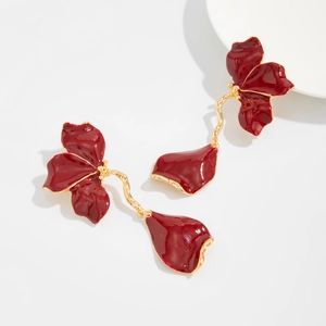 Detailed close-up of glossy red enamel flower petals and golden vine metal earrings