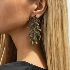 Gros plan de boucles d'oreilles feuilles dorées vintage avec strass noirs sur mannequin