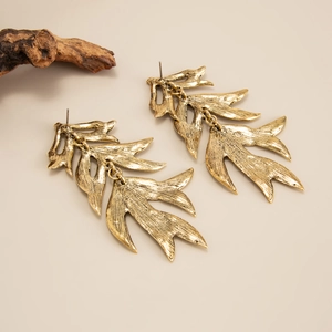 Détail de boucles d'oreilles feuilles dorées avec texture brossée mate sur bois