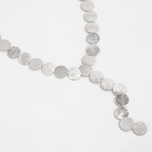 Macro detail of brushed silver geometric discs on a long fringe necklace for women