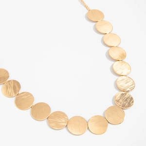 Macro detail of golden metal disc necklace with brushed texture and minimalist geometric design