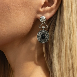 Détail de boucles d'oreilles argentées style montre de poche avec pierre noire et gravure