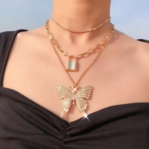 Close-up of layered gold necklace with butterfly pendant and lock charm on a model