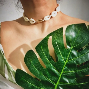 Handmade shell choker necklace with a gold accent piece worn by a model in tropical sun