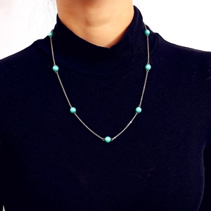 Detalle de collar de cadena dorada con perlas turquesas sobre fondo de punto negro