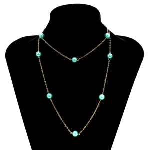 Primer plano de un collar de cadena dorada de doble capa con perlas verde claro en busto