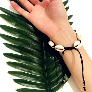 Detail of handmade cowrie shell bracelet with adjustable black cord and gold beads
