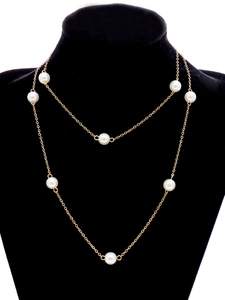 Detalle de un elegante collar de cadena dorada con perlas blancas en un soporte de joyas negro