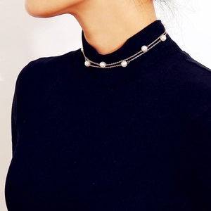 Primer plano de un elegante collar de doble capa dorado con perlas sobre suéter negro