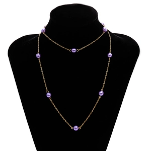 Detalle de un elegante collar de cadena dorada con perlas púrpuras en un busto negro