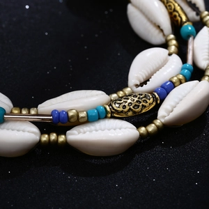Detail of bohemian seashell necklace with blue beads and gold engraved metal spacers