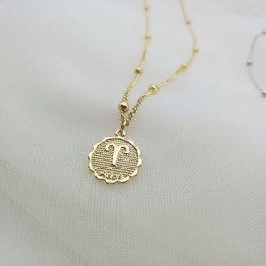 Dettaglio di una collana zodiacale Ariete dorata con bordo in pizzo su rete bianca