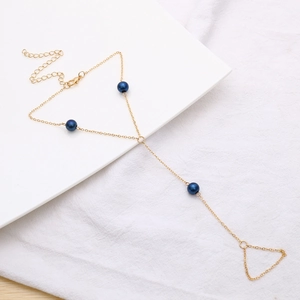 Detalle de una pulsera de dedo dorada con tres perlas azul oscuro y cierre de langosta