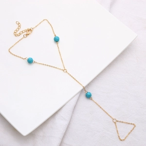 Detalle de una pulsera de dedo dorada con tres cuentas de turquesa y una cadena delicada