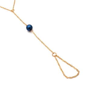 Detalle de una pulsera de anillo dorada con una perla azul oscuro en una cadena fina de oro