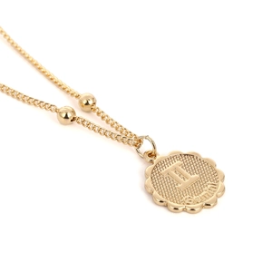 Nahaufnahme des goldenen Gemini-Sternzeichenanhängers mit Gittertextur und Perlenkette