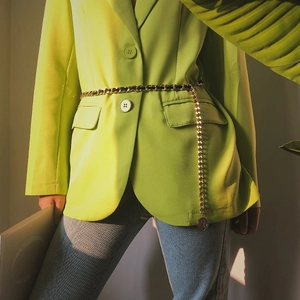 Detail of layered gold metal waist chain with coin pendant on green blazer