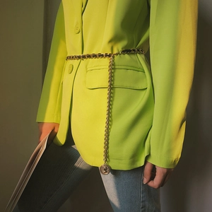 Detail of layered gold waist chain with metal rings and embossed coin pendant on green suit