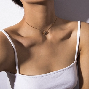 Close-up of minimalist gold butterfly pendant necklace on collarbone with artistic shadow