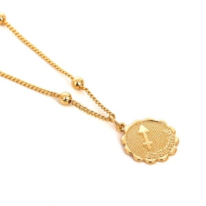 Makro-Detail des goldenen Schütze-Anhängers mit Wellenrand und feiner Perlenkette