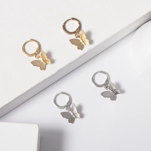 Detail of gold and silver butterfly hoop earrings with brushed metallic texture on white stand