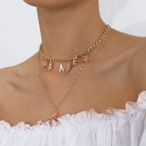 Close-up of layered BABE letter and pink butterfly pendants on gold-plated cuban chain