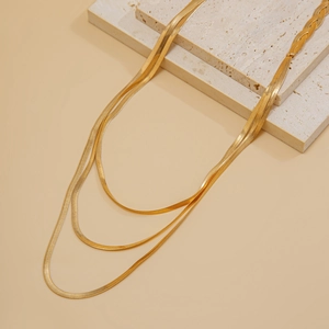 Detailed view of triple-layered golden flat snake chain necklaces on stone tiles