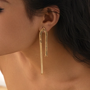 Detail of gold snake chain U-shaped earrings showing flexible metallic texture on model