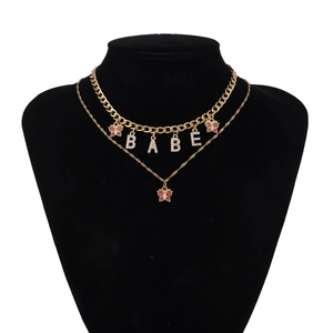 Detail of double-layer gold necklace with BABE letters and pink butterfly charms