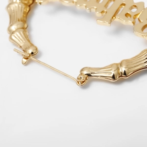 Makroaufnahme von goldenen Bamboo-Creolen mit Baby-Schriftzug und feiner Textur