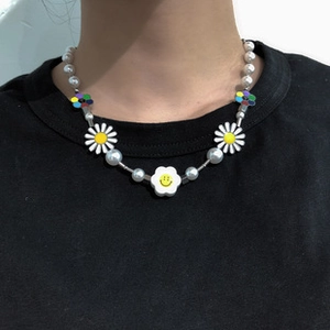 Detail of O-chain necklace with white pearls, daisy charms, and a yellow smiley face pendant