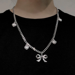 Detail of silver cuban chain necklace featuring heart charms and a 3D bow pendant