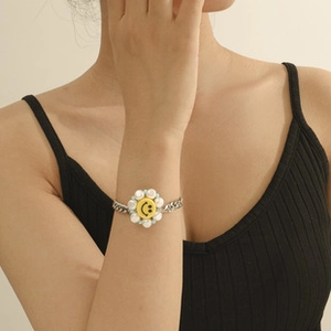 Close-up of a silver Cuban chain bracelet with a yellow smiley face and white pearls